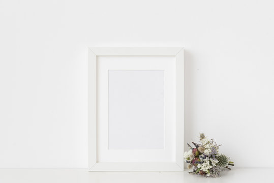 Minimal white a5 portrait frame mockup with small bouquet of dried flowers on white wall background. Empty frame, poster mock up for presentation design. Template frame for text, lettering, modern art