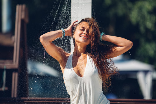 Heat and refreshment concept. Water drops falling on attractive woman. Young beautiful brunette girl taking shower on beach Sexy lady in bikini enjoys shower