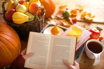 Reading in the autumn day.Autumn books.Autumn reading. book and tea,pumpkin, basket with apples, physalis, yellow maple leaves on a wooden table.Cozy autumn mood