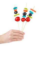 Hand hold three skewers with cheese, tomato and olives