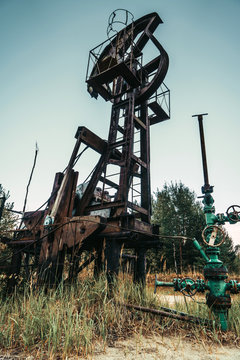 Old rusty pump jack in the oilfield situated in the beautiful forest. Environmental pollution. Oil and gas concept. 