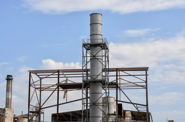 Sugar factory under construction, metal chimney with platforms and other elements of construction, another pipe and equipment in the background