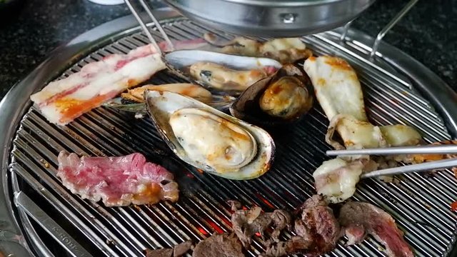 People cooking mussels, shrimp, slices bacon, meat on hot coals with chopsticks