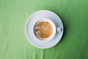 White ceramic cup of coffee on the green tablecloth.