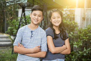 Portrait of cheerful teenage brother and sister folding arms and looking at camera