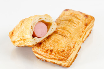 Tasty puff pastry dessert cut in half . Delicious pastries with sausage on light background. hot dog