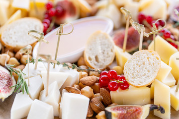 Cheese plate. Delicious cheese mix with baguette croutons, red currant, sweet figs, almond, honey on wooden table. Tasting dish on a wooden plate. Food for wine. Goat cheese, Parmesan, Gouda