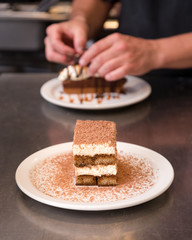 Tiramisu dusted with chocolate with a chocolate tart in the background.