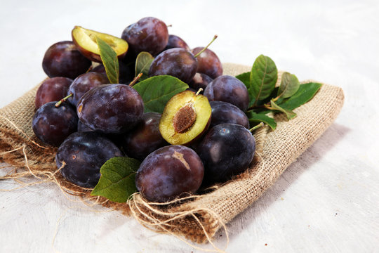 Plums on rustic background. Half of blue plum fruit. Many beautiful plums with leaves