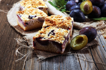 Rustic plum cake on wooden background with plums around.