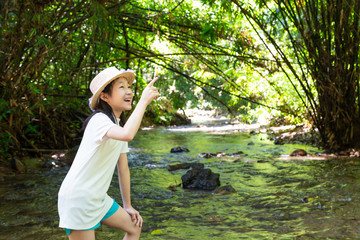 Asian girl in forest at stream,cute little girl studying and learning nature,natural forest background, girl having fun in trip near waterfall,smiling lovely,happy childhood