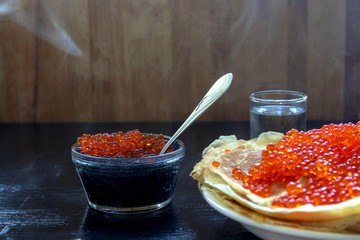 traditional thin Russian pancakes with red caviar on a dark rustic wooden background