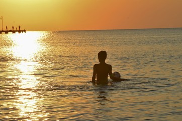 Fototapeta premium Young boy looking standing in the sea and looking at the sunset
