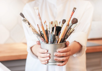 Different brushes in metal bucket with artist hands, selective focus