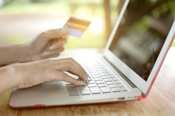 Close up hand of Asian woman using credit card for online shopping payment with laptop computer on blurred garden background, technology and Business concept