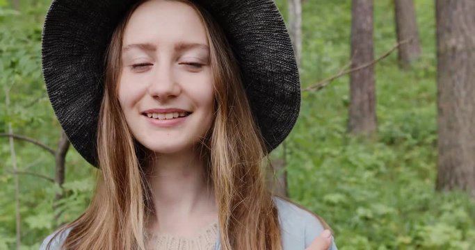 Close up Portrait of Beautiful Blonde Girl Smiling in a Nature setting in a hat. Student blue eyed hipster woman hiking and exploring the forest. Standing in woodland area