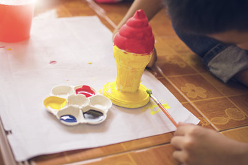 Children use brush to painting plastic ice cream cone with painting plate and bottle of water, art learning.