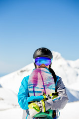 Fototapeta na wymiar Photo of young tourist girl in helmet looking into camera with snowboard in hands on background of snow mountains