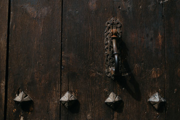 An ancient metal door knocker on the old wooden door with metal rivets in Spain. Chocolate color