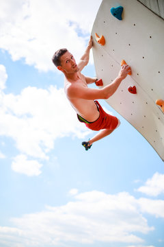 Photo of athlete looking at camera practicing on wall for rock climbing against blue sky with clouds