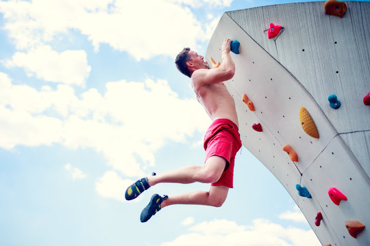 Photo of sportive man balancing on wall for climbing against cloudy sky