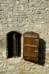 A rustic shuttered window with ornate security bars set in a stone wall in Pujols, Lot-et-Garonne, France. This historic village is a member of "Les Plus Beaux Villages de France" association.