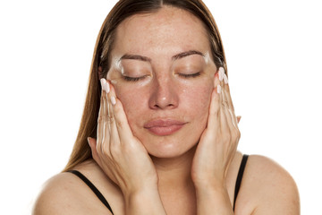 beautiful middle-aged woman applying moisturizer on her face on white background