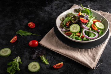 Vegetable salad with fresh lettuce, tomatoes and cucumber in white plate on black background