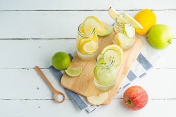 Green and yellow lemon with  green and red apples in soda bottles on cutting bord and white table