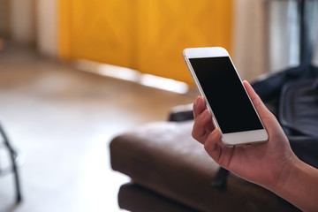 Mockup image of hands holding white mobile phone with blank black screen in cafe