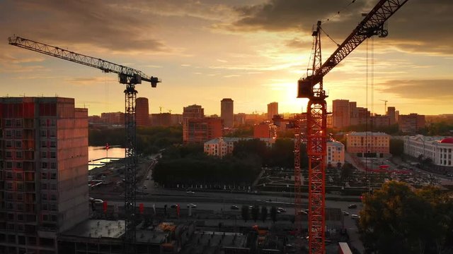 Aerial view of construction cranes silhouettes against sunset sky background. 4K UHD.