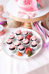  A festive table with desserts of pink color. Merengi, cakes, strawberries, marshmallows, flowers and sweets on a pink tablecloth
