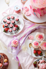  A festive table with desserts of pink color. Merengi, cakes, strawberries, marshmallows, flowers and sweets on a pink tablecloth