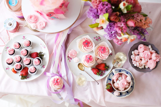  A festive table with desserts of pink color. Merengi, cakes, strawberries, marshmallows, flowers and sweets on a pink tablecloth