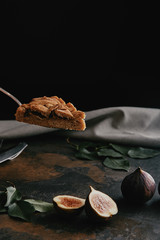 close up view of piece of pie on cake server and figs on dark grungy surface with black background