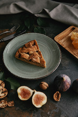 Fototapeta premium close up view of fresh figs and homemade pie on plate on dark grungy tabletop