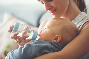 Mother, feeding her baby boy from bottle, sitting on the couch at home