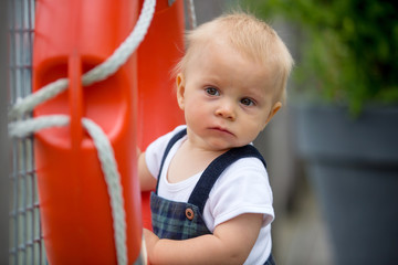 Sweet toddler baby boy, playing with plastic orange saving belt by the railing fence