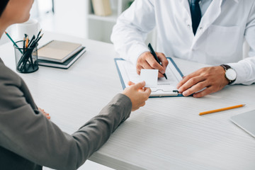 cropped image of patient giving id card to doctor to fill insurance claim form in clinic