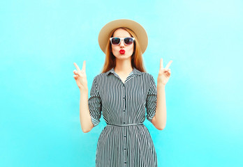 Fashion woman with red lips sends an air kiss in summer round straw hat on blue background