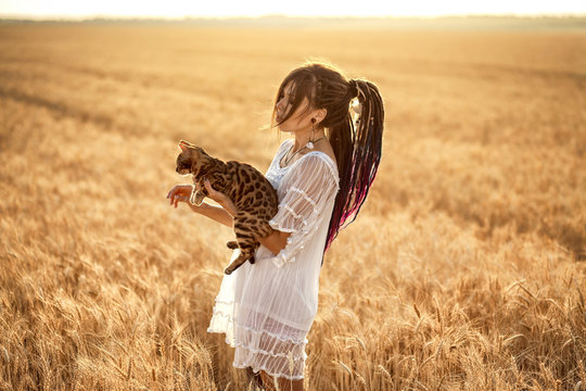 sunset photo shoot of a girl with dreadlocks in a white dress in wheat with a cat