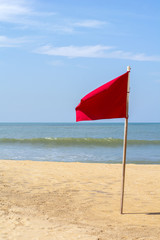 Red flag on the beach with a very calm ocean in the sunny day
