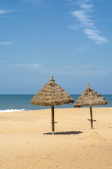 Two parasols on the beach, made of straw, near the water in the sunny day
