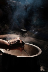 Woman's hand with rings mixing something mystical in a pot with vapor on the dark background