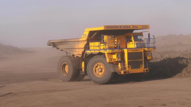 Gigantic trucks go around the bend. Huge mining truck rides on a quarry. The truck rides on off-road raising clouds of dust. Close up.