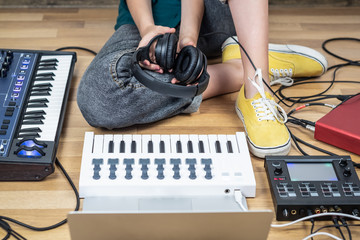 Female musician sits in a home studio with modern electronic instruments. Young woman producing modern indie music on synthesizer and digital controllers
