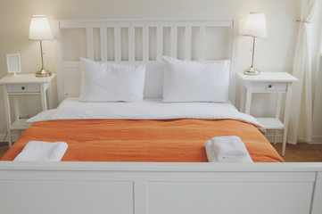 The hotel has a bedroom interior. White bed, orange bedspread, floor lamps on the bedside tables
