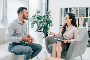 smiling psychiatrist with clipboard talking with happy patient in office