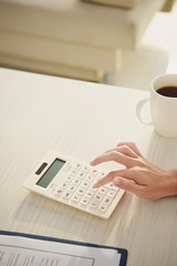 cropped view of woman counting finances on calculator at table with cup of coffee