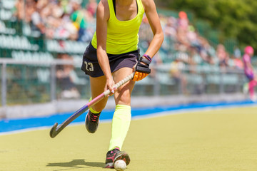 Young girl playing field hockey running with stick and ball